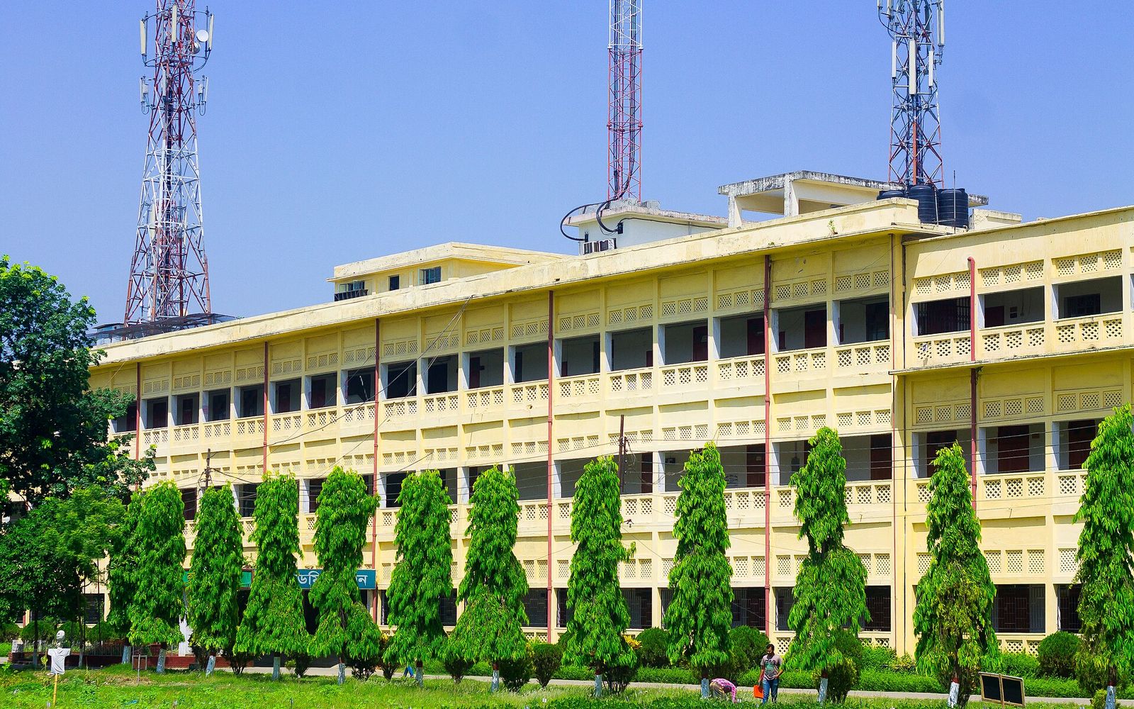Yellow academic building behind a row of trees at Sher e Bangla Agricultural University in Dhaka