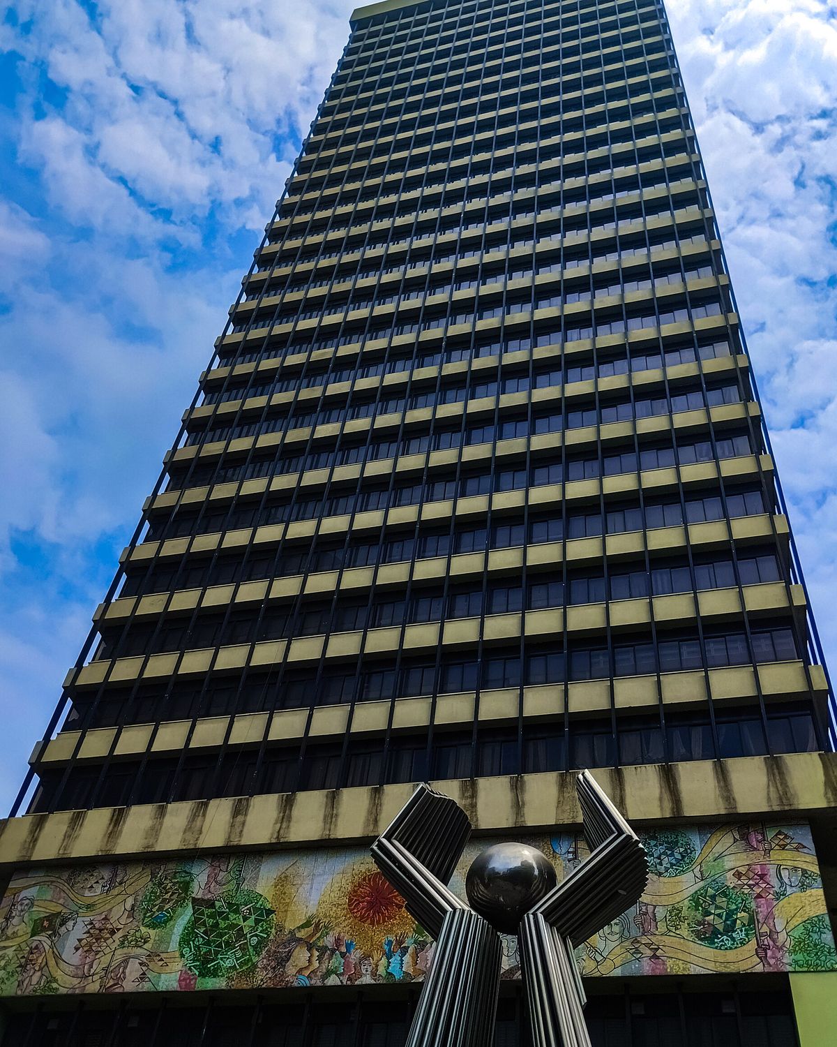 Bangladesh Bank's main building in Motijheel, Dhaka, a tall tower seen from below with a mural and a steel sculpture at its base