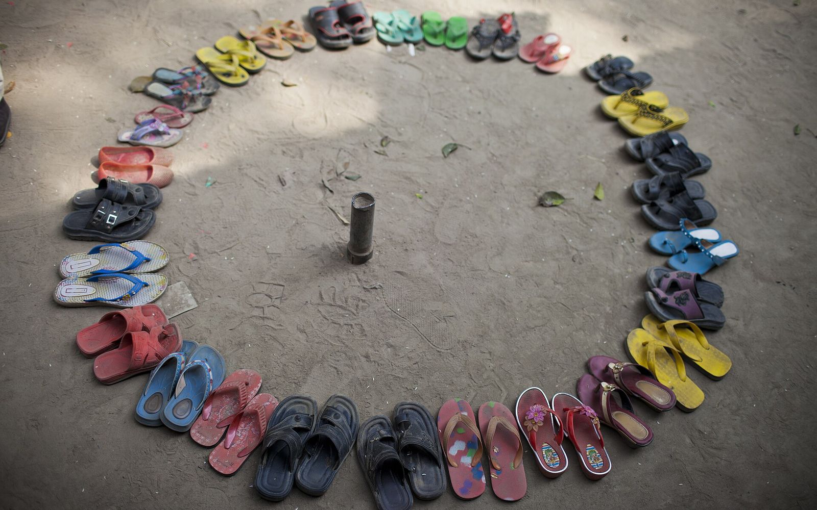 Children's sandals arranged in a circle on a dirt floor outside a BRAC school classroom in Bangladesh