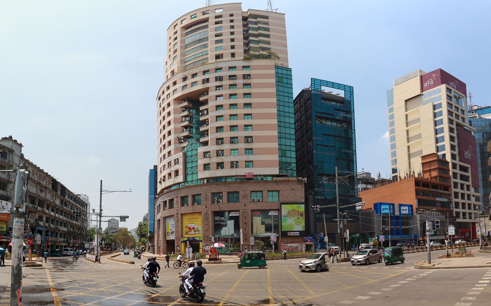 Office towers at a junction on Gulshan Avenue in Dhaka, with cars, motorbikes and CNG auto rickshaws crossing in the foreground