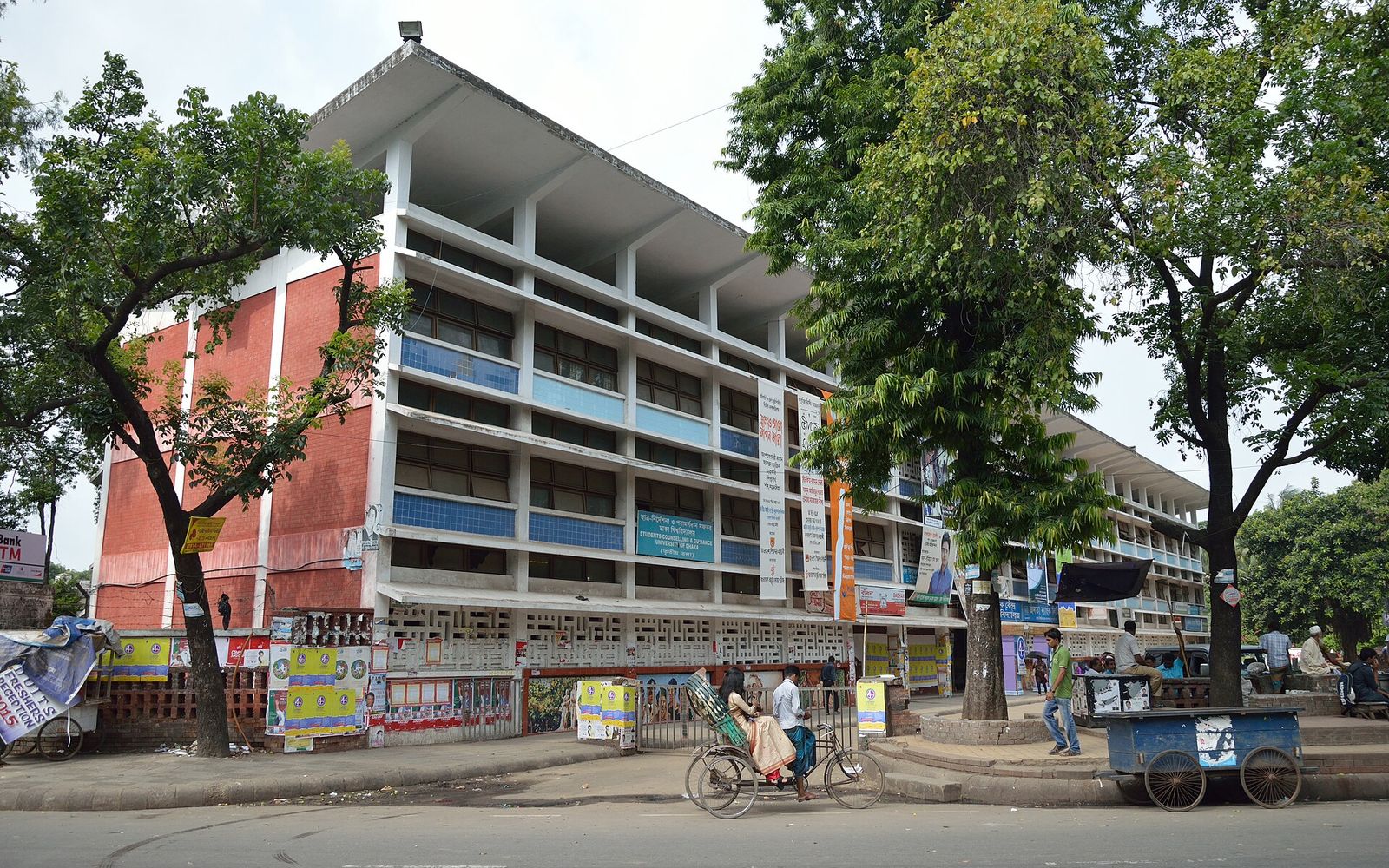 The Teacher Student Centre building at the University of Dhaka seen from the road, with trees in front and a rickshaw passing